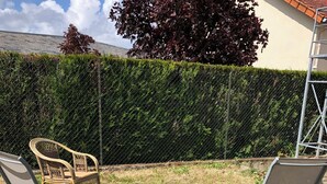 Dos sillas al aire libre con estructura metálica y asientos de tela, ubicadas sobre una zona cubierta de césped, con una valla de malla metálica y un seto al fondo.