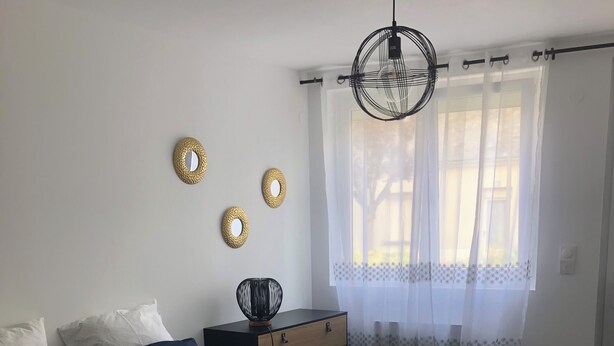 Un dormitorio con cama, mesita de noche y ventana con cortinas ligeras.