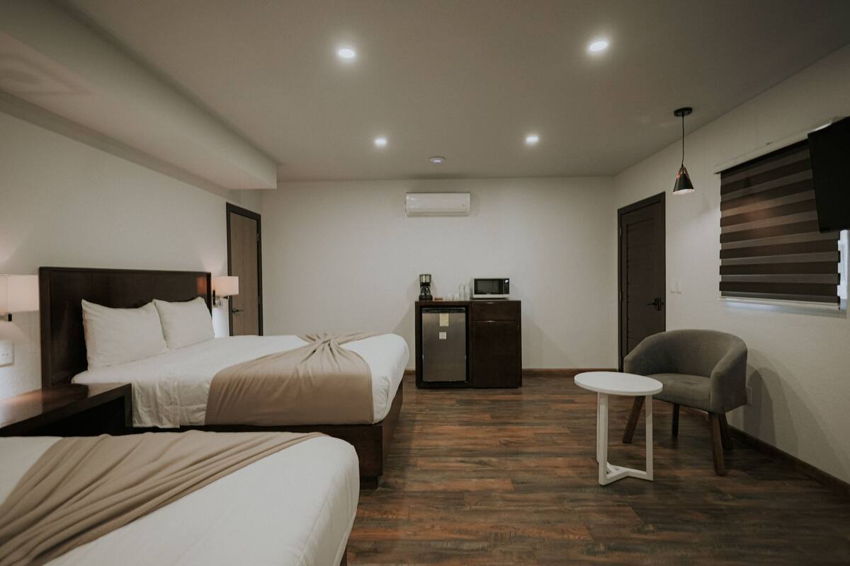 Ein Hotelzimmer mit zwei Betten, einem kleinen Tisch, einem Sessel, einem Fernseher und einer Minibar.