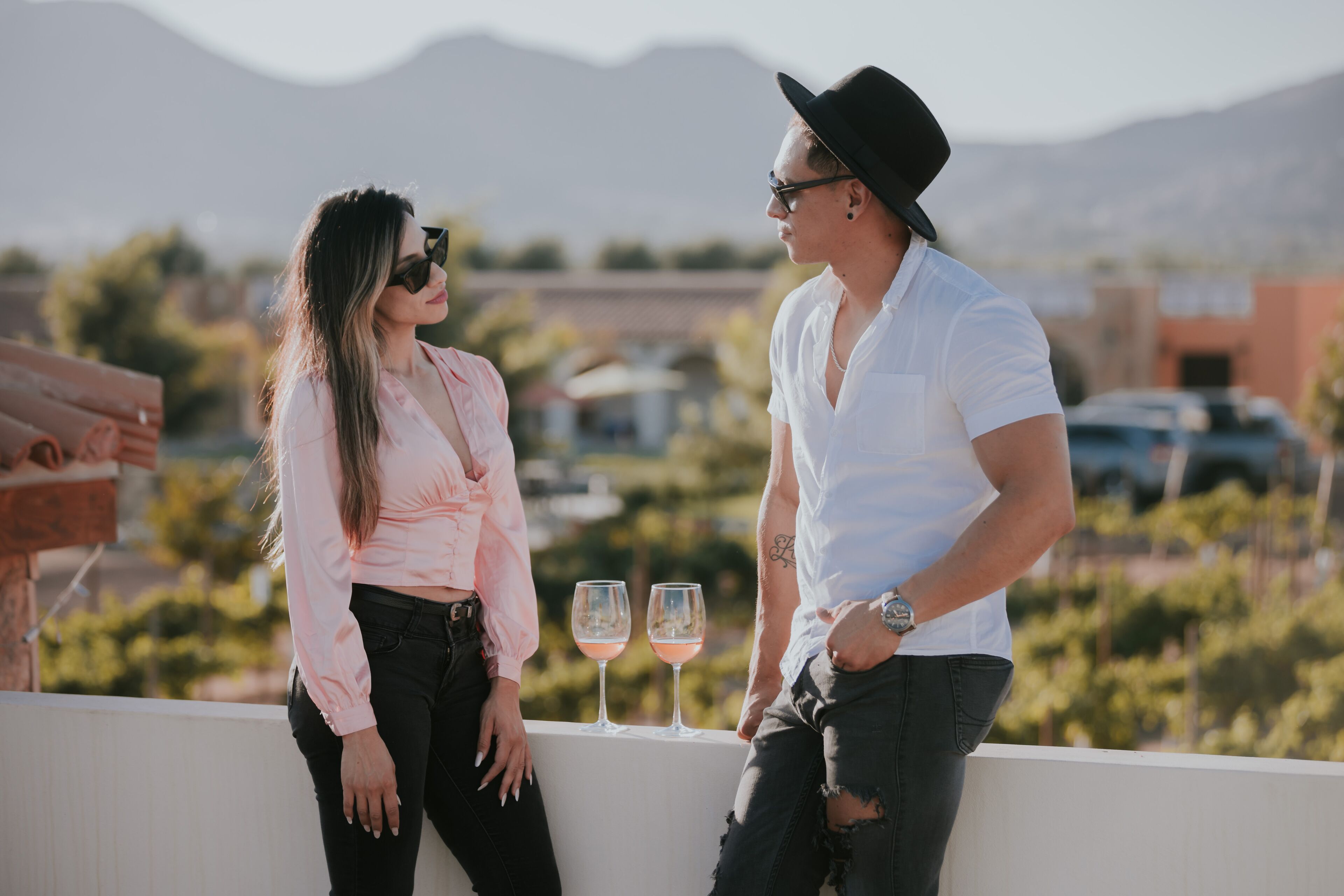 Una pareja parada en un balcón, con vistas a viñedos y montañas al fondo.