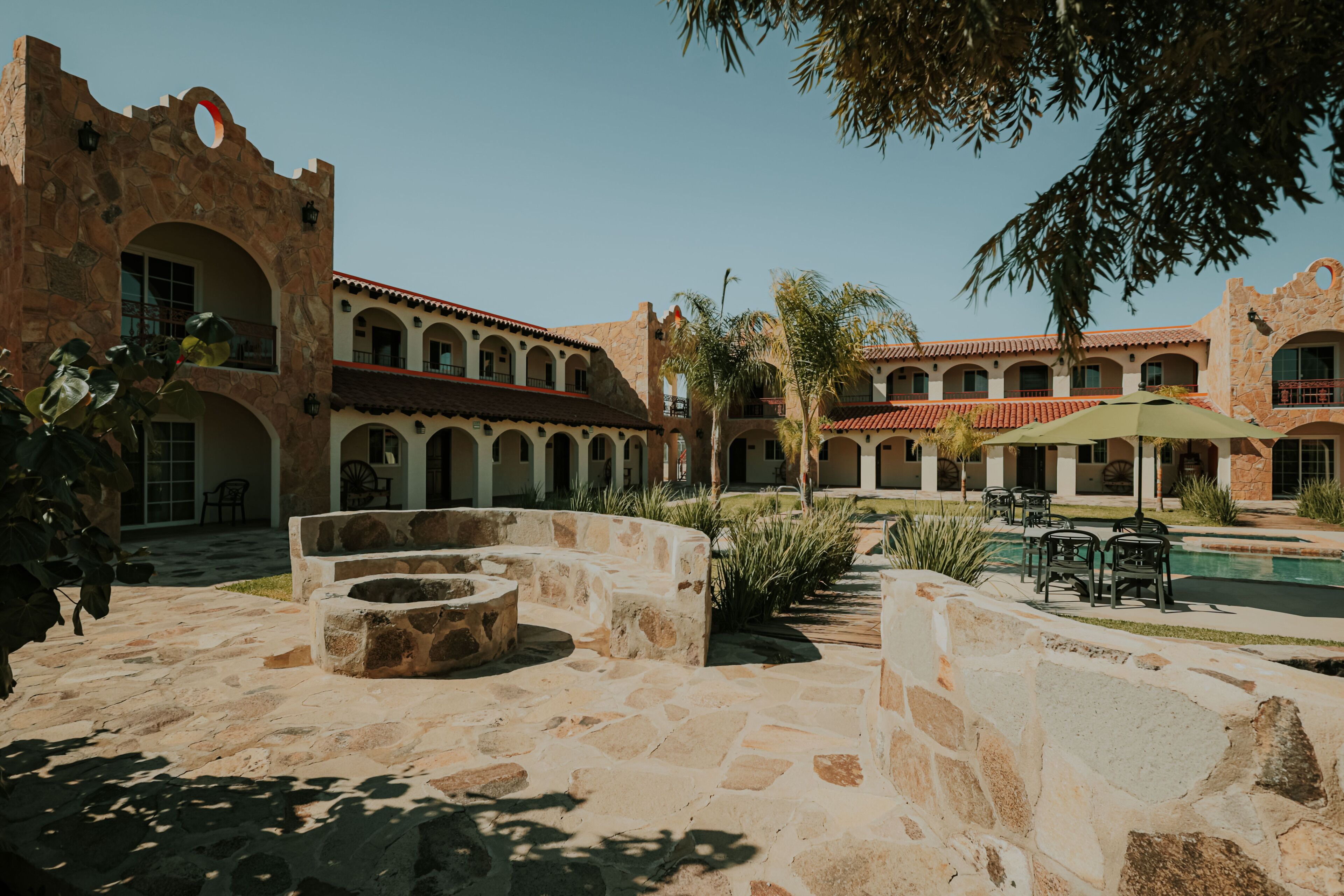 A courtyard with stone seating, a pool, and a building with arches and balconies.