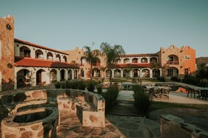 A courtyard with stone benches, a pool, and a building with arches and a red-tiled roof.