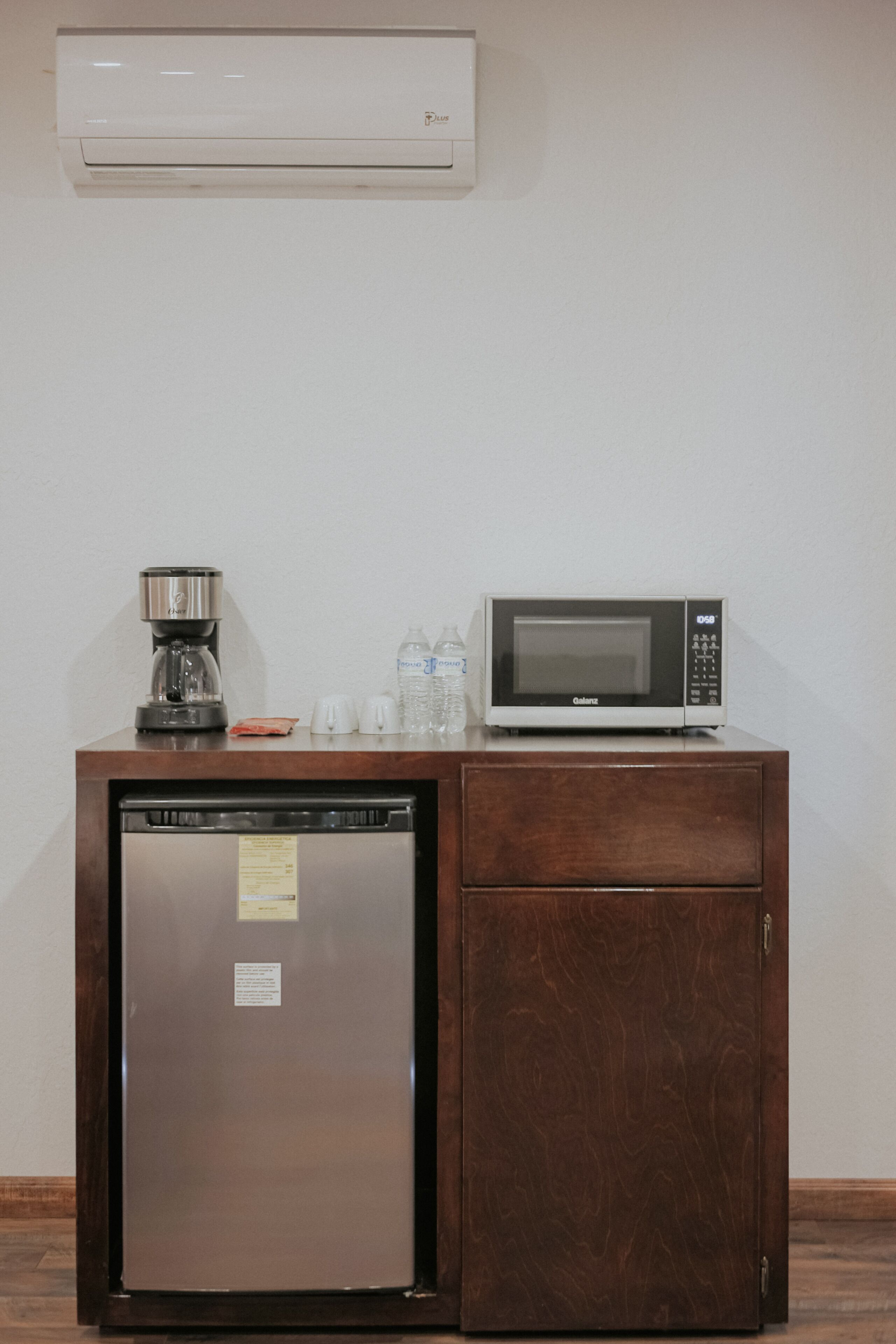 A compact kitchenette with a refrigerator, microwave, coffee maker, and water bottles.