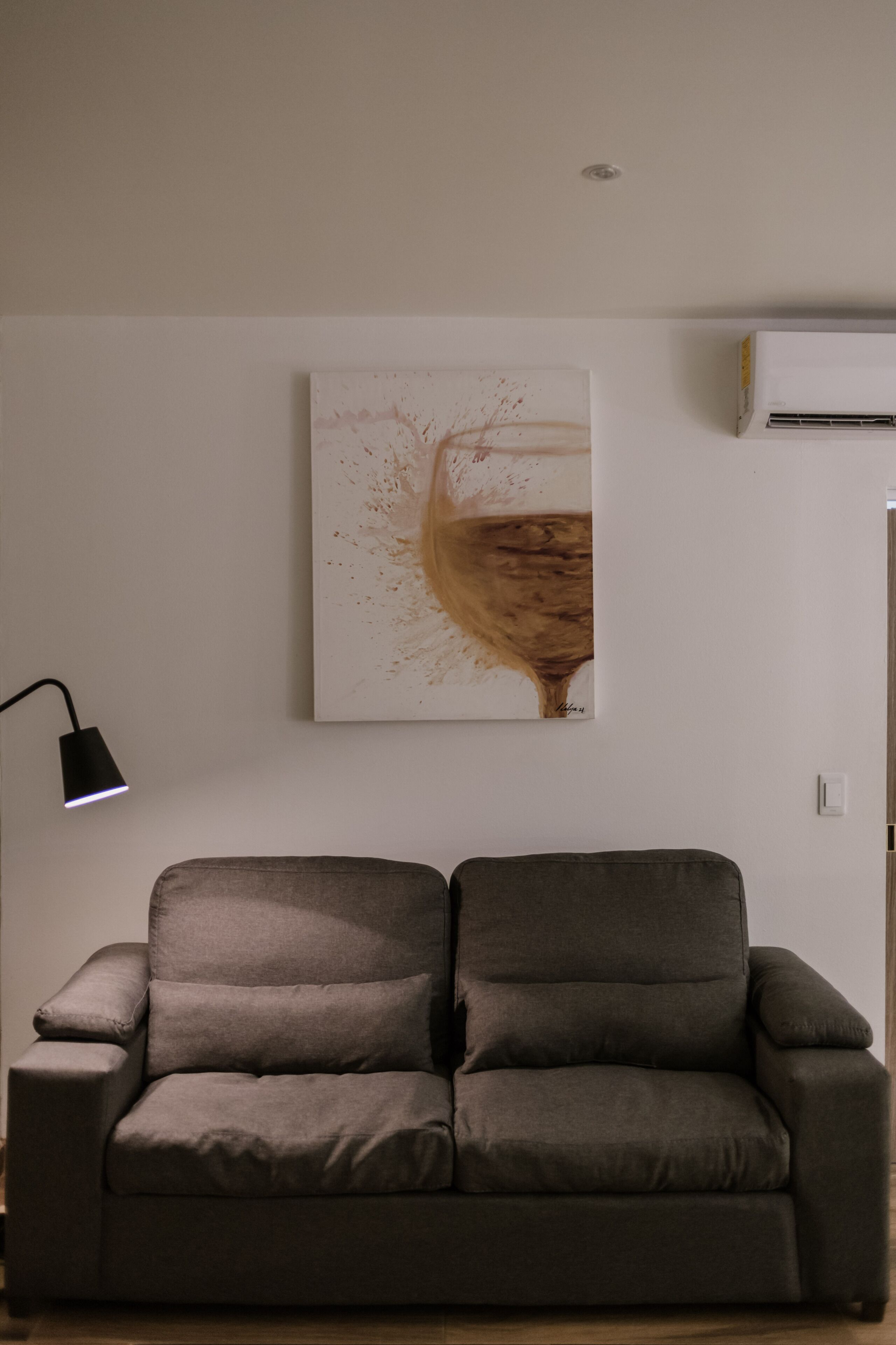 Ett modernt vardagsrum med en grå soffa, en tavla som hänger på väggen och en taklampa.