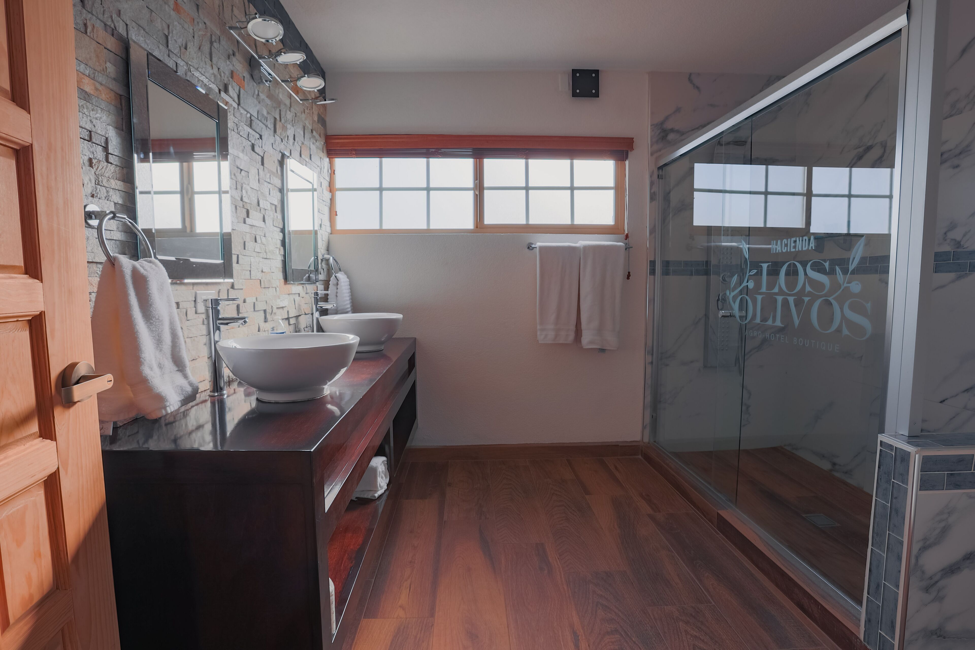 A modern bathroom with a wooden vanity, two sinks, a large mirror, and a glass shower enclosure.