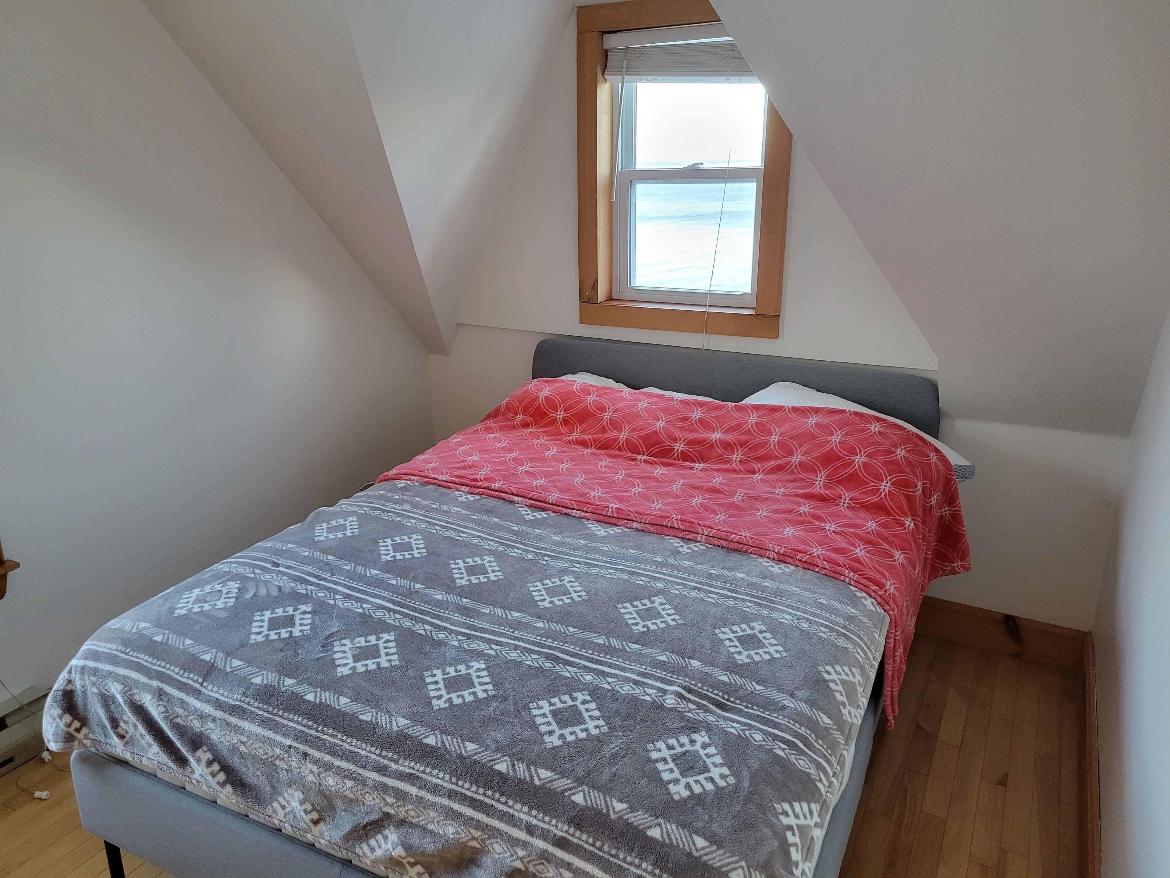 A small, single-bed room with a sloped ceiling and a window.