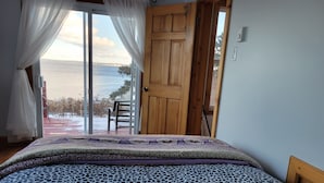 Un dormitorio con cama, una puerta de madera y vista al mar a través de un ventanal.
