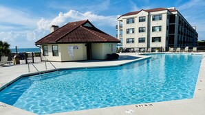 A swimming pool with a tiled deck, a small building with a red roof, and a multi-story building in the background.