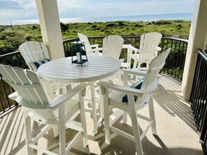 Ein weißer Außenbereich mit Sitzgelegenheiten, einem runden Tisch und Stühlen mit Blick auf Strand und Meer.