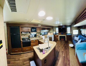 Une cuisine compacte pour camping-car, équipée d’une cuisinière, d’un four à micro-ondes, d’un évier et d’un petit coin repas.