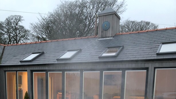 A hot tub with a control panel, surrounded by small potted plants, and a house with large sliding glass doors and a clock on the roof. - Modern Converted Stables in the heart of Pembrokeshire (Wiston)