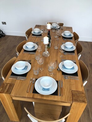 A dining table set with white plates, blue napkins, and clear glassware, surrounded by wooden chairs.