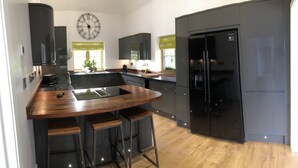 A modern kitchen with a curved wooden island, black cabinets, and a black refrigerator. - Modern Converted Stables in the heart of Pembrokeshire (Wiston)