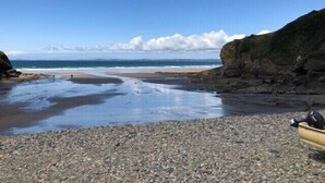 A pebble beach with a boat on the right and a rocky cliff on the left. - Modern Converted Stables in the heart of Pembrokeshire (Wiston)