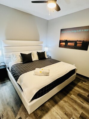 A neatly made bed with a headboard, a ceiling fan, and a wall-mounted picture of a bridge. - Top of Stillwater by Okoboji Luxury Rentals (Arnolds Park)