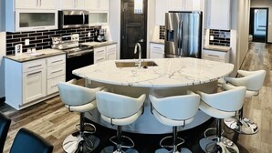 Una cocina moderna con armarios blancos, electrodomésticos de acero inoxidable y una isla central con taburetes de bar.