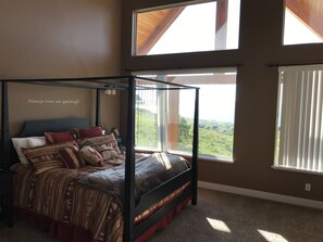 Ein Himmelbett mit Blick auf eine grüne Landschaft durch große Fenster.