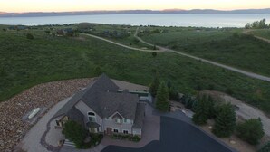 A large, two-story house with a stone foundation, a driveway, and a small pond in the foreground. - Bear Lake Cabin w/ lots of privacy and amazing Lake View (Fish Haven)