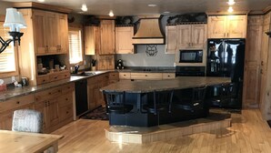 A modern kitchen with wooden cabinets, a central island with bar stools, a microwave, and a refrigerator. - Bear Lake Cabin w/ lots of privacy and amazing Lake View (Fish Haven)