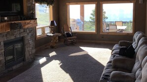 A spacious living room with a stone fireplace, a large window offering a view of the outdoors, a ceiling fan, and a plush sofa. - Bear Lake Cabin w/ lots of privacy and amazing Lake View (Fish Haven)