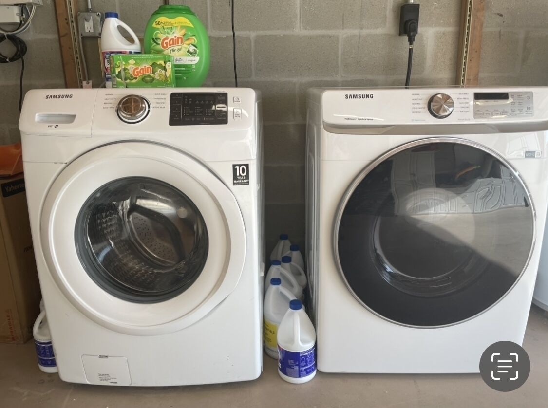 Two white Samsung front-loading washing machines with a 10-year warranty label, placed next to each other with detergent bottles nearby.