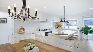 Eine moderne Küche mit weißen Schränken, einem Holztisch und einer zentralen Kochinsel mit Sitzgelegenheiten.