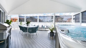Eine Außenterrasse mit Whirlpool, Grill und Sitzgelegenheit mit Topfpflanzen.