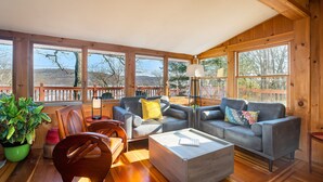 A spacious living area with a wooden ceiling, large windows, and a view of the outdoors.