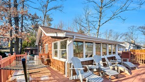 A wooden deck with Adirondack chairs and a glass-enclosed porch.