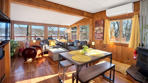 A cozy cabin interior with wooden walls, a fireplace, and a large window with curtains.