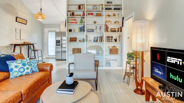 A modern living room with a leather sofa, a bookshelf, a dining area, and a TV displaying streaming services. - Quick Bike Ride to Central Austin from Quiet 1BD (Austin)