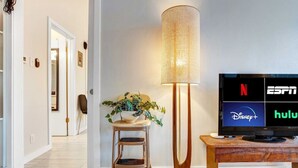 A modern living room with a flat-screen TV displaying streaming services, a floor lamp, and a wooden chair. - Quick Bike Ride to Central Austin from Quiet 1BD (Austin)