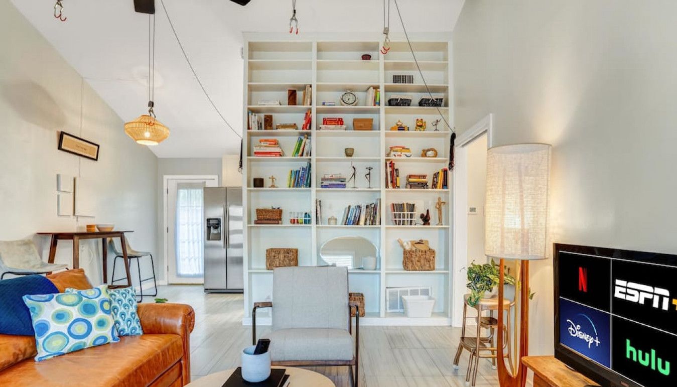 A modern living room with a leather sofa, a bookshelf, a dining area, and a TV displaying streaming services.