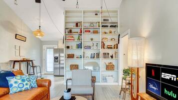 A modern living room with a leather sofa, a bookshelf, a dining area, and a TV displaying streaming services.