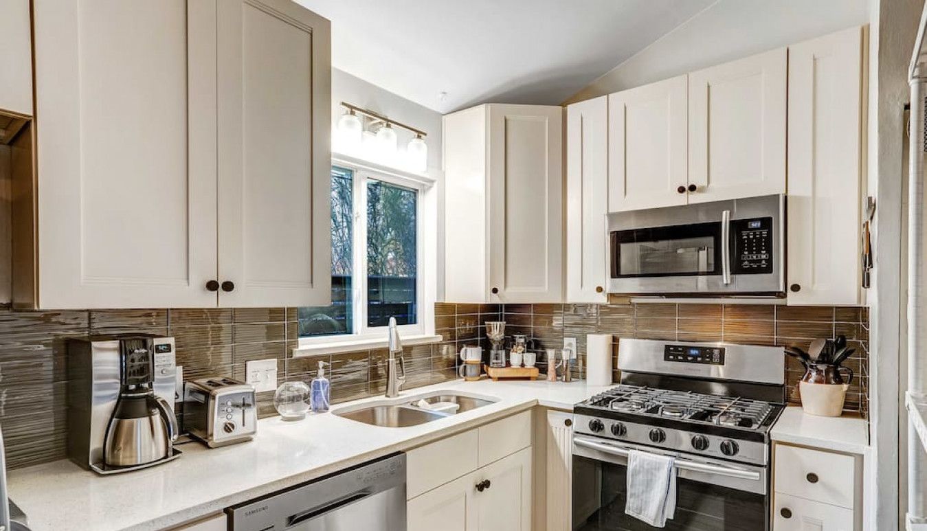 A modern kitchen with white cabinets, stainless steel appliances, and a window providing natural light.