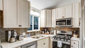 A modern kitchen with white cabinets, stainless steel appliances, and a window providing natural light.
