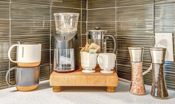 A kitchen counter with a coffee maker, a coffee pot, a grinder, and two coffee cups.