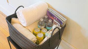Una cesta tejida con una toalla blanca, varias latas de bebidas y una pila de revistas.