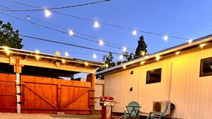 An outdoor patio area with a fire pit, wooden furniture, and string lights.