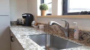 A kitchen with a stainless steel sink, a coffee maker, a potted plant, and a bottle of hand soap.