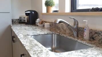 A kitchen with a stainless steel sink, a coffee maker, a potted plant, and a bottle of hand soap.