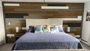 Quarto com cabeceira de madeira, cama com colcha azul e várias almofadas.