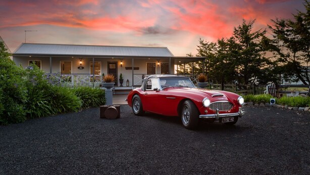 A red classic car parked in front of a house with a porch and outdoor seating area. - Hampton Cottage - " A Place To Call Home" (Port Albert)