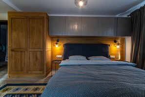 A bedroom with a wooden wardrobe, a bed with a blue patterned bedspread, and two wall-mounted lamps.