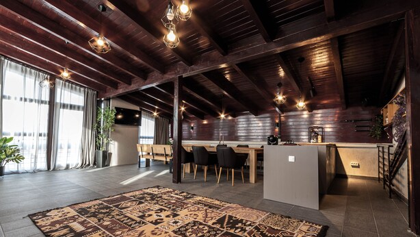 Una cocina amplia con comedor, vigas de techo de madera e iluminación moderna.