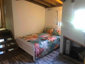 Ein kleines Zimmer mit einem Einzelbett, einer blumigen Bettdecke, einem Holz-Kopfteil und einer fest eingebauten Bank am Fußende des Bettes.