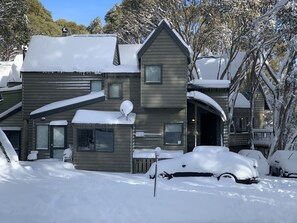 Een tweelaags houten huis met een sneeuwbedekte dak en oprit, een schotelantenne, en een bord waarop staat dat parkeren alleen toegestaan is voor bewoners van Faithful's.
