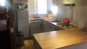 A compact kitchen with a microwave, refrigerator, dishwasher, and a red kettle on the stove. - Charming Alpine Chalet 'Faithfulls' at Dinner Plain - Pet Friendly (Dinner Plain)