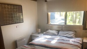 A bedroom with a bed, a nightstand, a lamp, and a window with a view of trees. - Charming Alpine Chalet 'Faithfulls' at Dinner Plain - Pet Friendly (Dinner Plain)