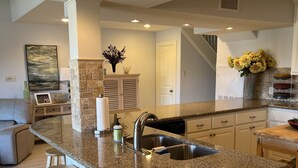 Una cocina con encimera de granito, pileta de acero inoxidable y taburetes de madera.